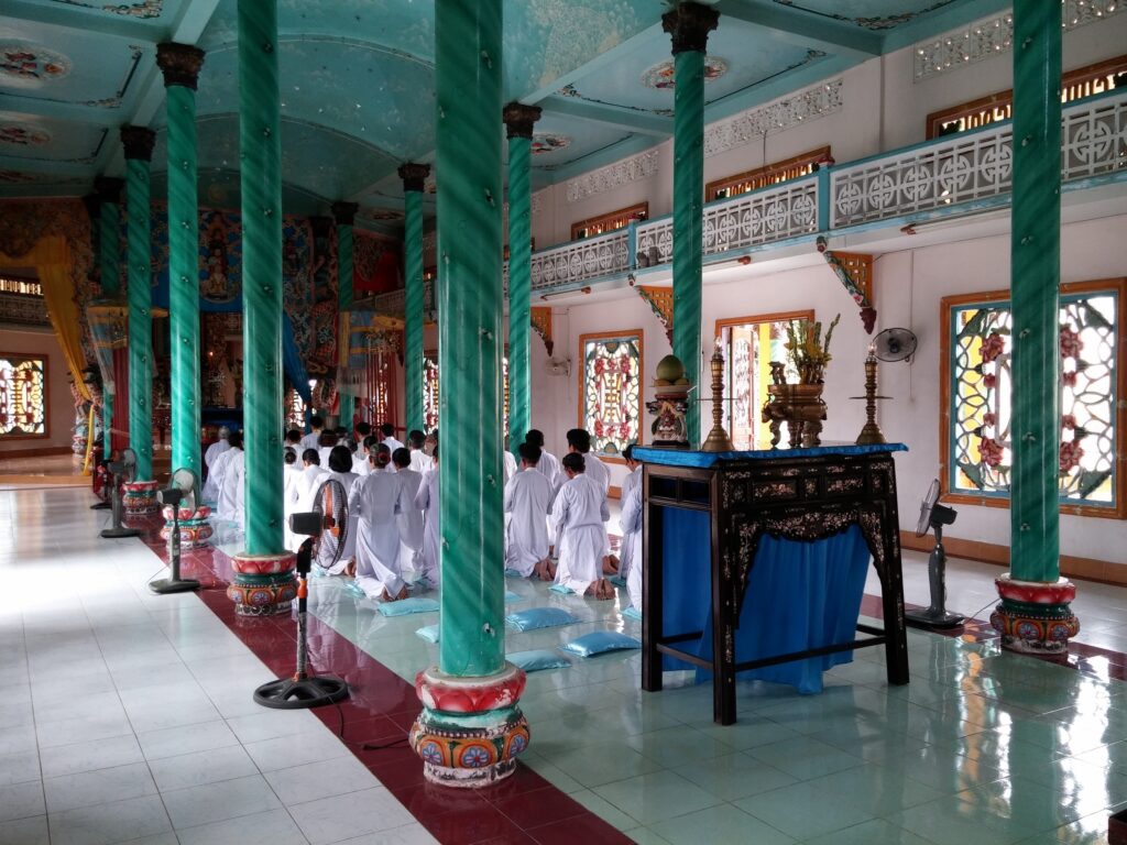 Teal pillars and people in prayer at an imperial building in Hue, Vietnam